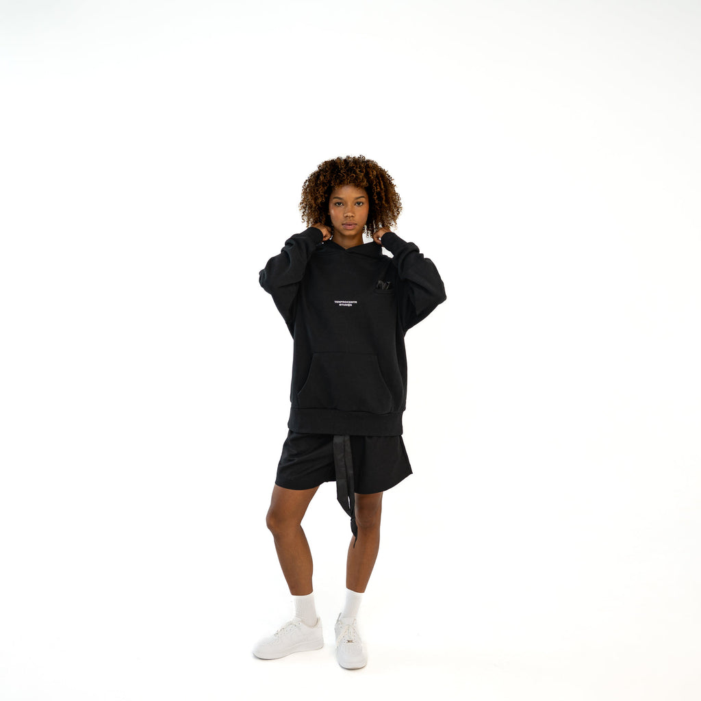 TenProcentr EN MARGE Heavyweight Hoodie in Schwarz, Vorderansicht am Model mit Brust-Logo und Kapuze