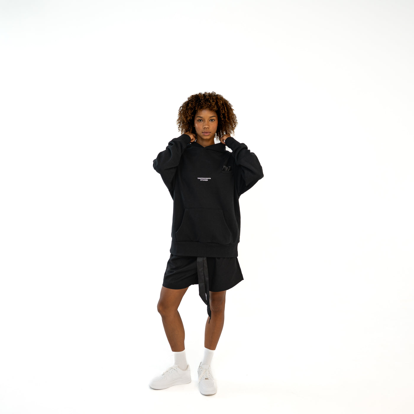 TenProcentr EN MARGE Heavyweight Hoodie in Schwarz, Vorderansicht am Model mit Brust-Logo und Kapuze