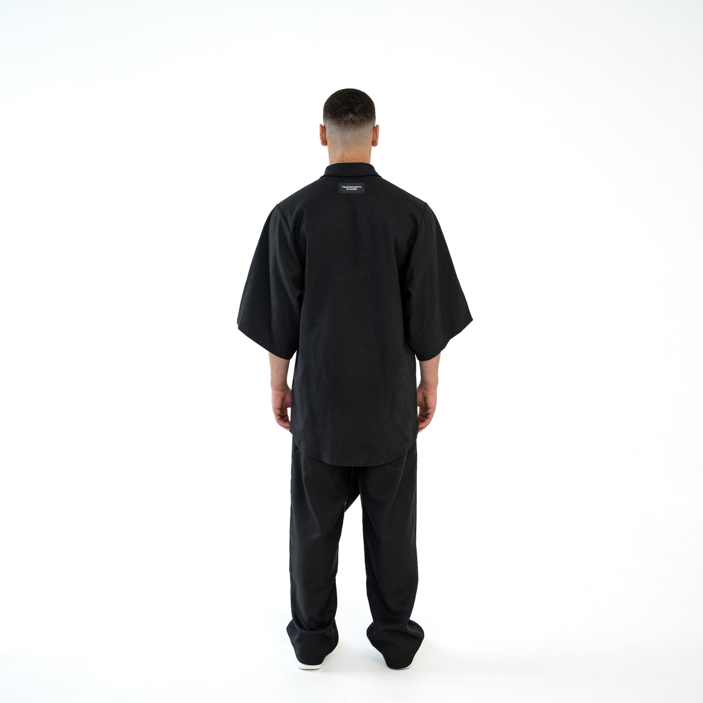 Rückansicht des schwarzen TenProcentr OUTFIELD Oversized Shirts am Model mit TenProcentr Studios Label am Nacken