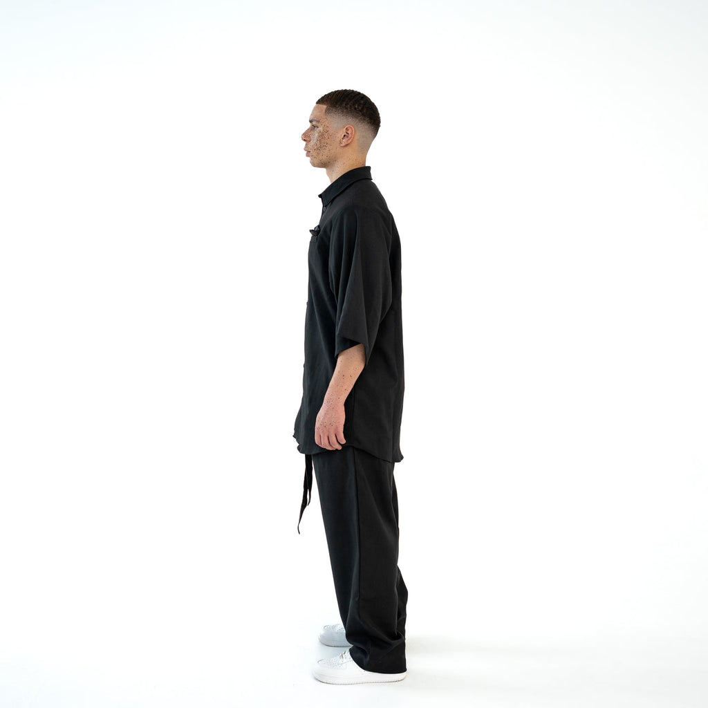 Seitenansicht des schwarzen TenProcentr OUTFIELD Oversized Shirts am Model, betont die oversized Passform und Ärmellänge