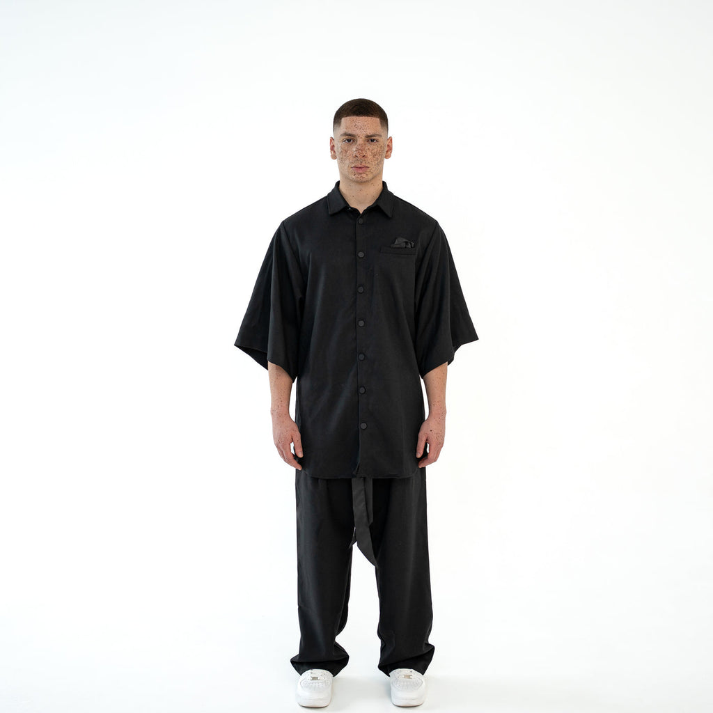 Model trägt das schwarze TenProcentr OUTFIELD Oversized Shirt in der Vorderansicht, geknöpft mit Brusttaschen-Detail