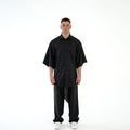 Model trägt das schwarze TenProcentr OUTFIELD Oversized Shirt in der Vorderansicht, geknöpft mit Brusttaschen-Detail