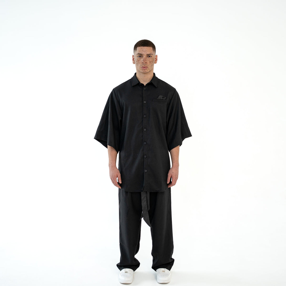 Model trägt das schwarze TenProcentr OUTFIELD Oversized Shirt in der Vorderansicht, geknöpft mit Brusttaschen-Detail